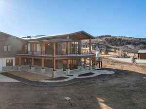 Back of house with a balcony, stairway, a patio area, and stone siding