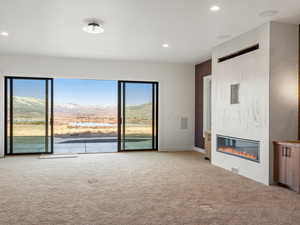 Unfurnished living room with a large fireplace, light carpet, a water and mountain view, and recessed lighting
