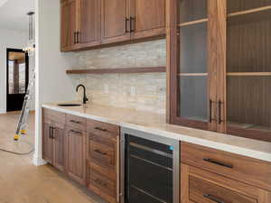 Bar with brown cabinets, beverage cooler, light wood-style floors, hanging light fixtures, and light stone countertops