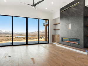 Unfurnished living room with a water and mountain view, a fireplace, light wood-style flooring, recessed lighting, and ceiling fan