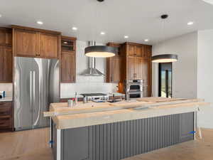 Kitchen with appliances with stainless steel finishes, an island with sink, decorative light fixtures, decorative backsplash, and brown cabinetry