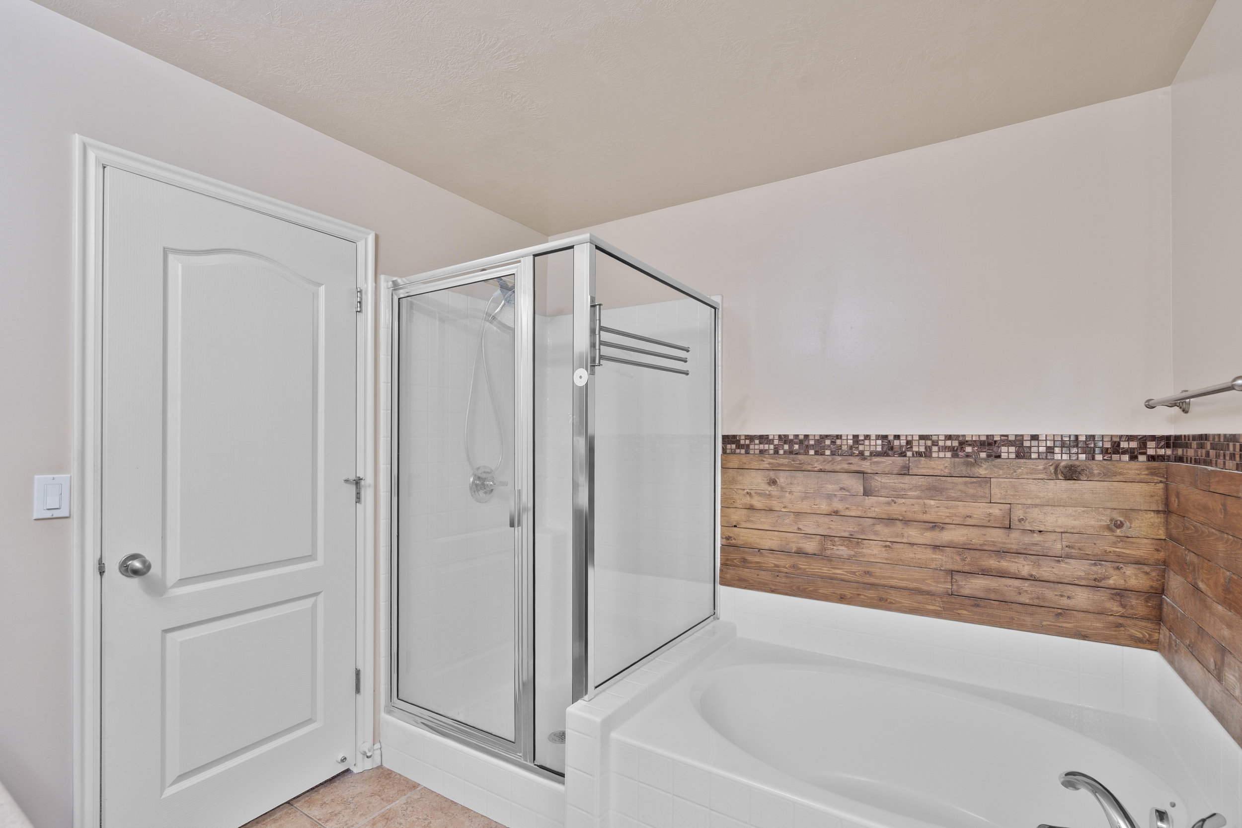 Owners/Master Bathroom featuring a garden tub, a shower stall, light tile patterned flooring, and a wainscoted wall