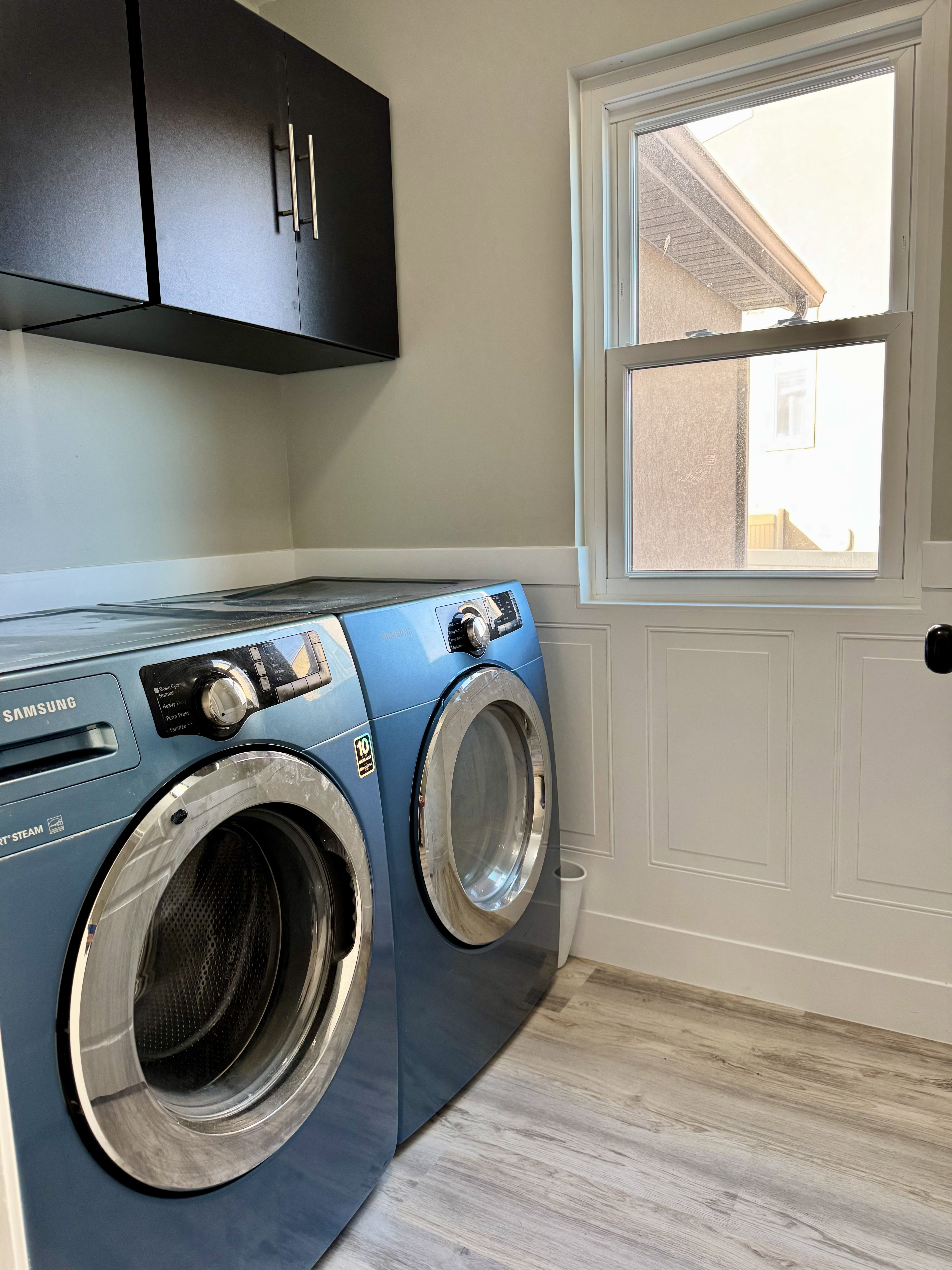 Laundry area with cabinet space, light wood finished floors, washer and clothes dryer, and wainscoting