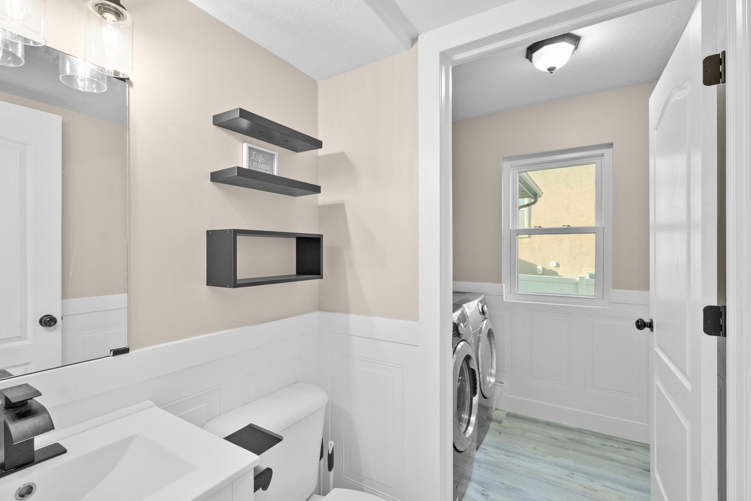 Half bathroom with a wainscoted wall, separate washer and dryer, light wood-style flooring, vanity, and a decorative wall