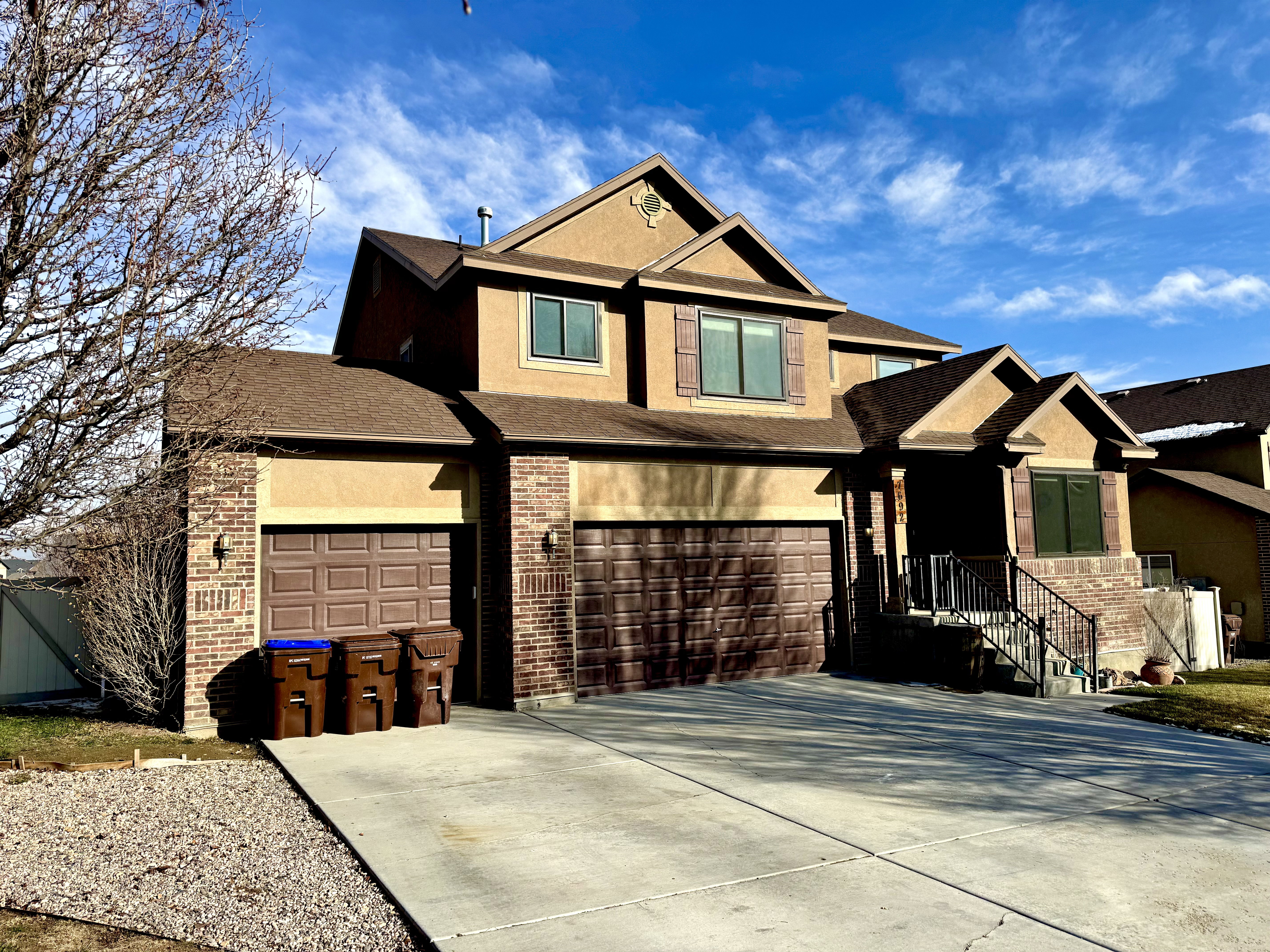 View of front of home with stucco siding, a shingled roof, concrete driveway, an attached garage, and brick siding