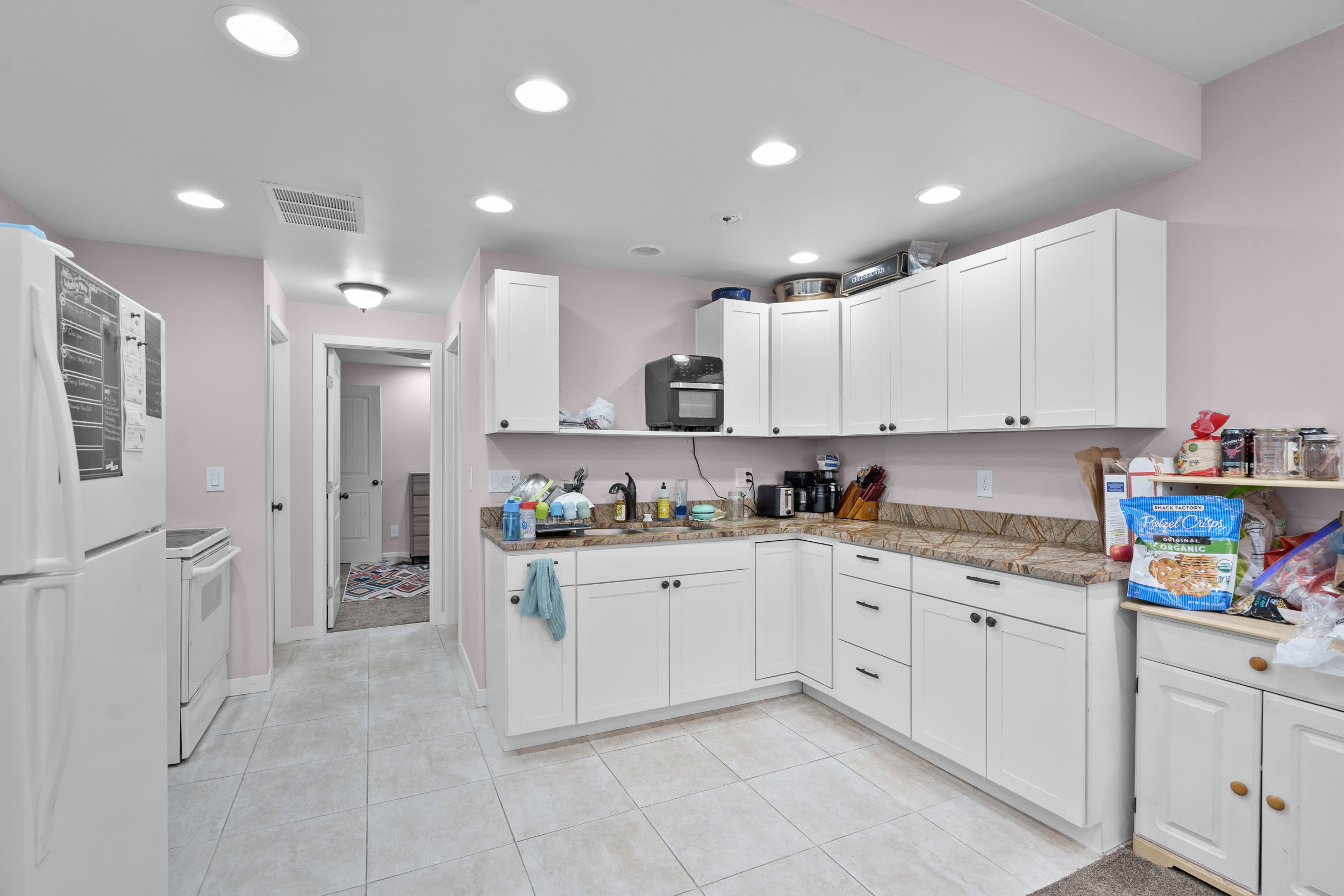 Kitchen featuring white appliances, white cabinets, light tile patterned floors, light stone counters, and recessed lighting