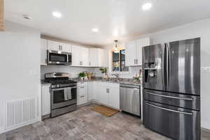Kitchen featuring appliances with stainless steel finishes, pendant lighting, white cabinetry, recessed lighting, and light wood finished floors