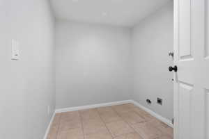 Washroom with electric dryer hookup and light tile patterned flooring