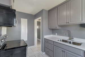 Kitchen with black microwave, electric range oven, light stone countertops, gray cabinets, and light marble finish floors