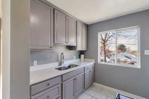 Kitchen with gray cabinetry, light marble finish flooring, and light stone counters