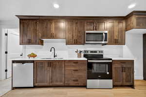 Kitchen with appliances with stainless steel finishes, light wood-style flooring, light stone counters, recessed lighting, and dark brown cabinets