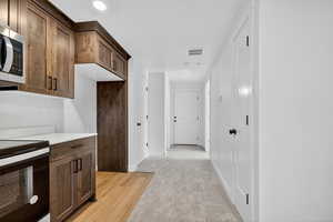 Kitchen with stainless steel appliances, light carpet, light stone counters, and dark brown cabinets