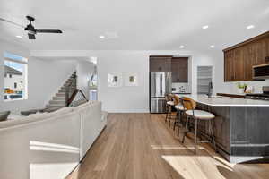 Kitchen featuring open floor plan, dark brown cabinets, stainless steel appliances, a breakfast bar, and a ceiling fan
