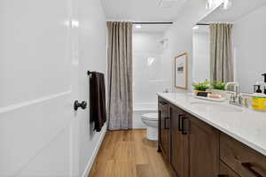 Full bath with shower / bath combination with curtain, vanity, and light wood-style floors