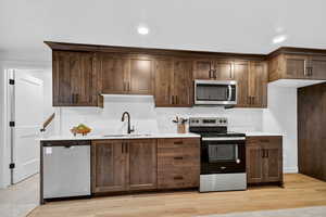 Kitchen with stainless steel appliances, light wood-style flooring, light stone counters, dark brown cabinets, and recessed lighting