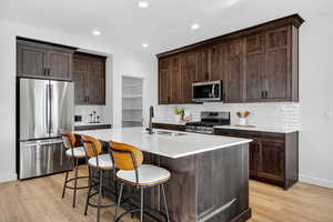 Kitchen with dark brown cabinets, stainless steel appliances, tasteful backsplash, a breakfast bar area, and light wood finished floors