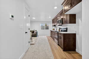 Kitchen with dark brown cabinetry, appliances with stainless steel finishes, recessed lighting, light wood finished floors, and light stone countertops