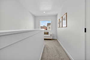 Hallway with light colored carpet and a textured ceiling
