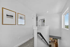 Hallway with an upstairs landing and light colored carpet