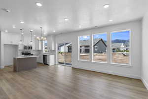 Kitchen featuring open floor plan, white cabinets, decorative light fixtures, light wood-style floors, and a kitchen island