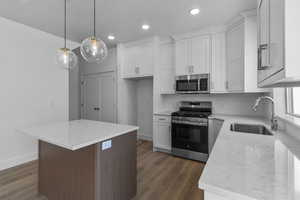 Kitchen with appliances with stainless steel finishes, light stone countertops, a center island, tasteful backsplash, and white cabinetry
