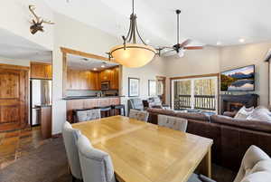 Dining room with a glass covered fireplace, ceiling fan, high vaulted ceiling, stone tile flooring, and recessed lighting
