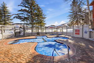 Snow covered pool with a community pool, a gate, a jacuzzi, and a patio