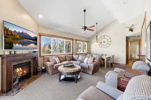 Living area featuring high vaulted ceiling, ceiling fan, a high end fireplace, and carpet flooring