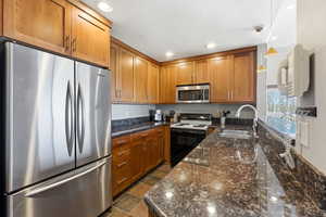 Kitchen with appliances with stainless steel finishes, dark stone counters, brown cabinets, decorative light fixtures, and recessed lighting