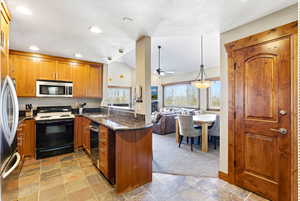 Kitchen with dark stone countertops, decorative light fixtures, open floor plan, vaulted ceiling, and appliances with stainless steel finishes