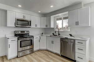 Kitchen featuring stainless steel appliances, white cabinetry, recessed lighting, light wood-type flooring, and light stone countertops