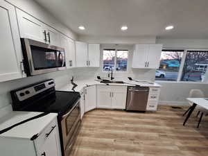 Kitchen with stainless steel appliances, white cabinets, light wood-type flooring, recessed lighting, and light stone counters