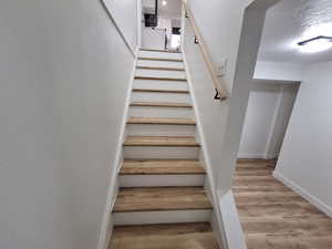 Stairs with wood finished floors and a textured ceiling
