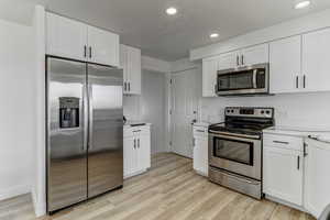 Kitchen featuring appliances with stainless steel finishes, white cabinetry, light wood-style floors, and recessed lighting