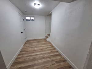 Hallway featuring a textured ceiling, light wood-type flooring, a textured wall, and stairs