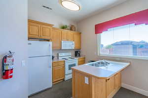 Kitchen with white appliances, light countertops, dark colored carpet, light brown cabinets, and a kitchen bar