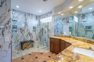 Full bath featuring a marble finish shower, double vanity, recessed lighting, tile walls, and stone wall