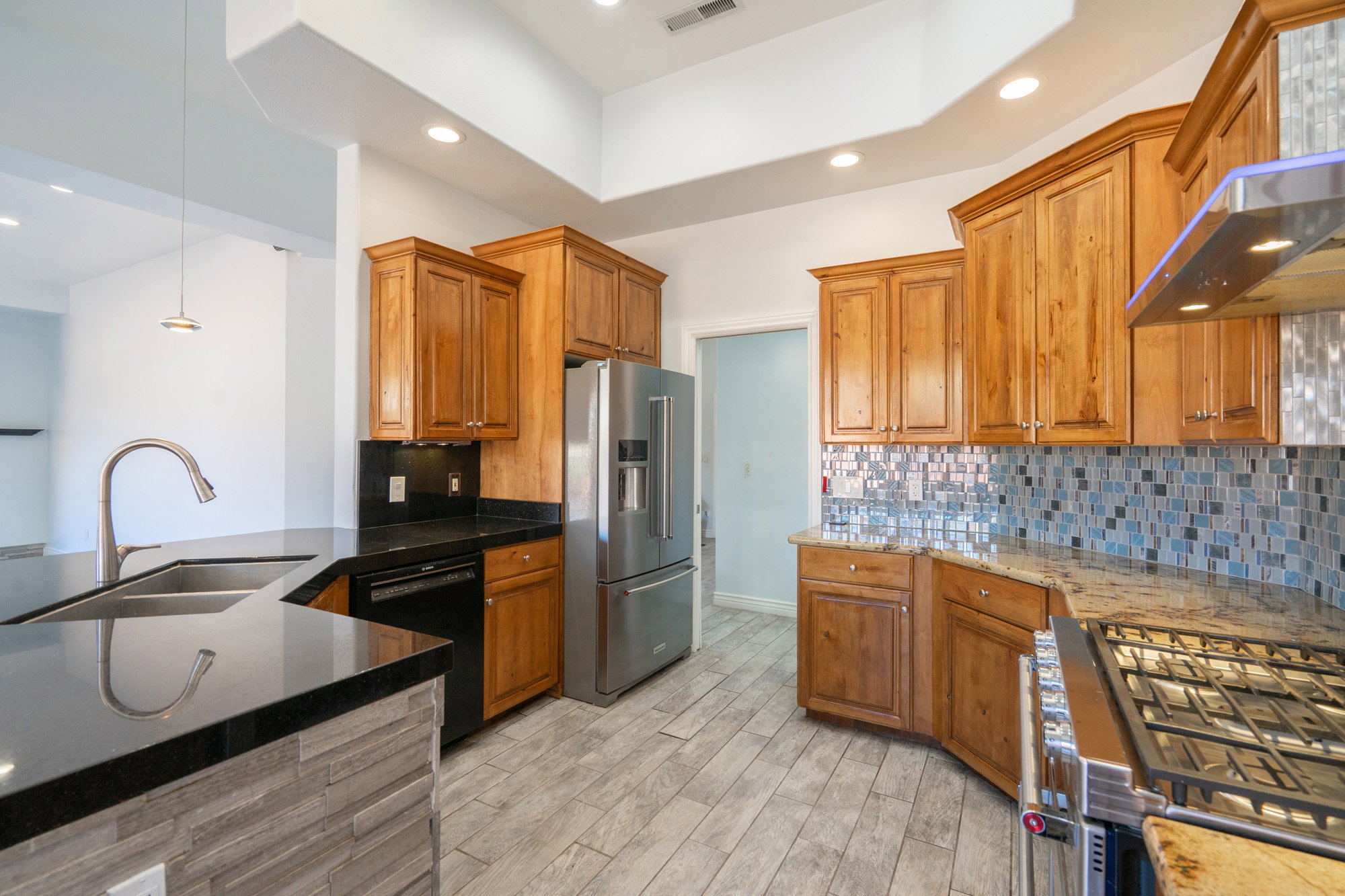 Kitchen featuring brown cabinets, appliances with stainless steel finishes, recessed lighting, dark stone countertops, and hanging light fixtures