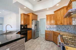 Kitchen featuring brown cabinets, appliances with stainless steel finishes, recessed lighting, dark stone countertops, and hanging light fixtures
