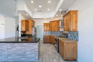 Kitchen with brown cabinetry, stainless steel appliances, a peninsula, decorative backsplash, and dark stone countertops