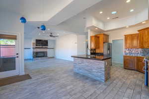 Kitchen with brown cabinets, decorative light fixtures, open floor plan, ceiling fan, and a peninsula