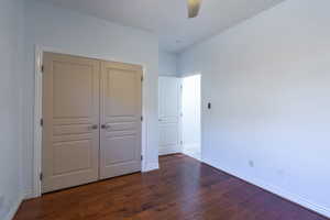 Unfurnished bedroom featuring dark wood-style flooring, a closet, and a ceiling fan