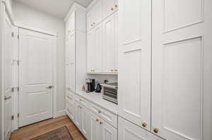 Bar area featuring white cabinetry, light wood-type flooring, and tasteful backsplash