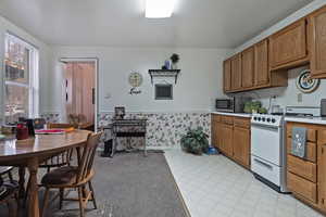 Kitchen with light flooring, light countertops, gas range gas stove, wainscoting, and brown cabinetry