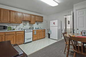 Kitchen featuring light countertops, white appliances, brown cabinetry, and light floors
