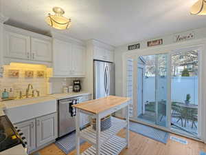 Kitchen with stainless steel appliances, a textured ceiling, tasteful backsplash, light wood-style floors, and white cabinets