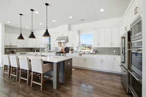 Kitchen with a kitchen island with sink, backsplash, a breakfast bar, decorative light fixtures, and recessed lighting