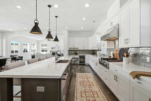 Kitchen featuring a breakfast bar, white cabinetry, hanging light fixtures, a large island with sink, and open floor plan
