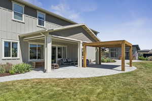 Rear view of property with board and batten siding, a patio area, a yard, and an outdoor living space