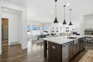 Kitchen with a kitchen bar, a chandelier, a center island with sink, dark wood-style flooring, and hanging light fixtures